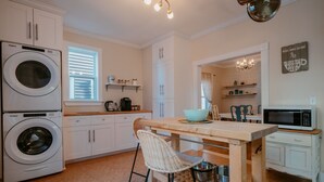 A compact kitchen with a built-in washer and dryer, a wooden island with bar stools, and a microwave on a small cabinet. - Downtown Heritage Home | 3 Bed + Backyard (St. John`s)