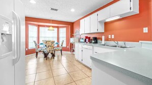 A kitchen with white cabinets, a countertop, and a sink. There is a dining area with a table and chairs. - Spring Hill Serenity:Cozy Escape (Spring Hill)