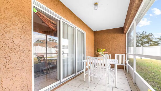 A balcony with a sliding glass door, white chairs, a small table, and a potted plant. - Spring Hill Serenity:Cozy Escape (Spring Hill)