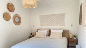 Een slaapkamer met een bed, twee nachtkastjes, een macramé wanddecoratie en een hangende rieten lamp.