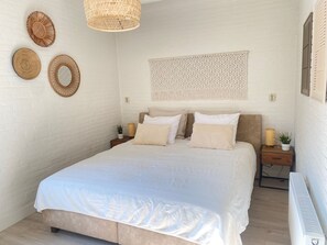 Ein Schlafzimmer mit einem Bett, zwei Nachttischen, einer Wanddekoration aus Makramee und einer Hängeleuchte aus Rattan.