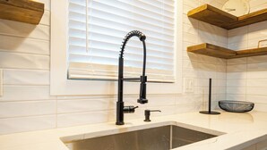 Una cocina con un lavamanos moderno, estanterías de madera y un ventanal con persianas.