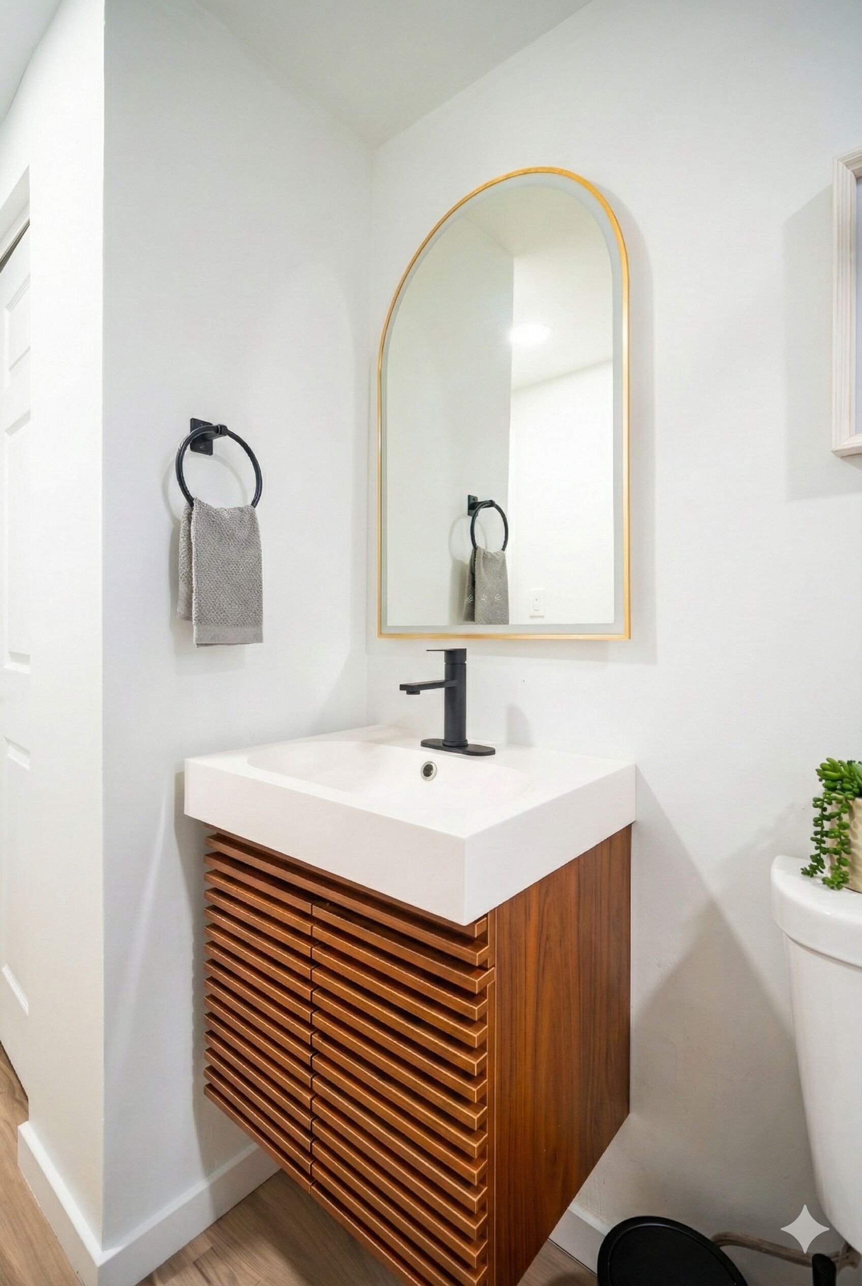 Une salle de bain moderne avec un meuble-lavabo blanc, un placard en bois, un robinet noir et un miroir avec un cadre doré.