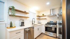 Una cocina moderna con armarios blancos, electrodomésticos de acero inoxidable, estanterías de madera y horno empotrado.