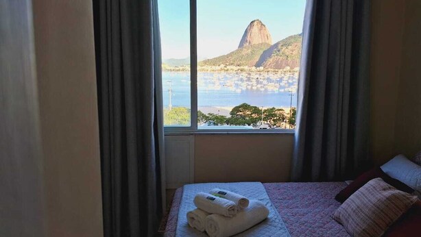 Ein Hotelzimmer mit Bett, einem Fenster mit Vorhängen und Blick auf Berg und Wasser.
