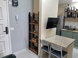A compact kitchen with a built-in TV, a small dining area with a table and chairs, and a shelf with decorative items. - Botafogo, Rio de Janeiro | Apartment with a view of Sugarloaf Mountain (Rio de Janeiro)