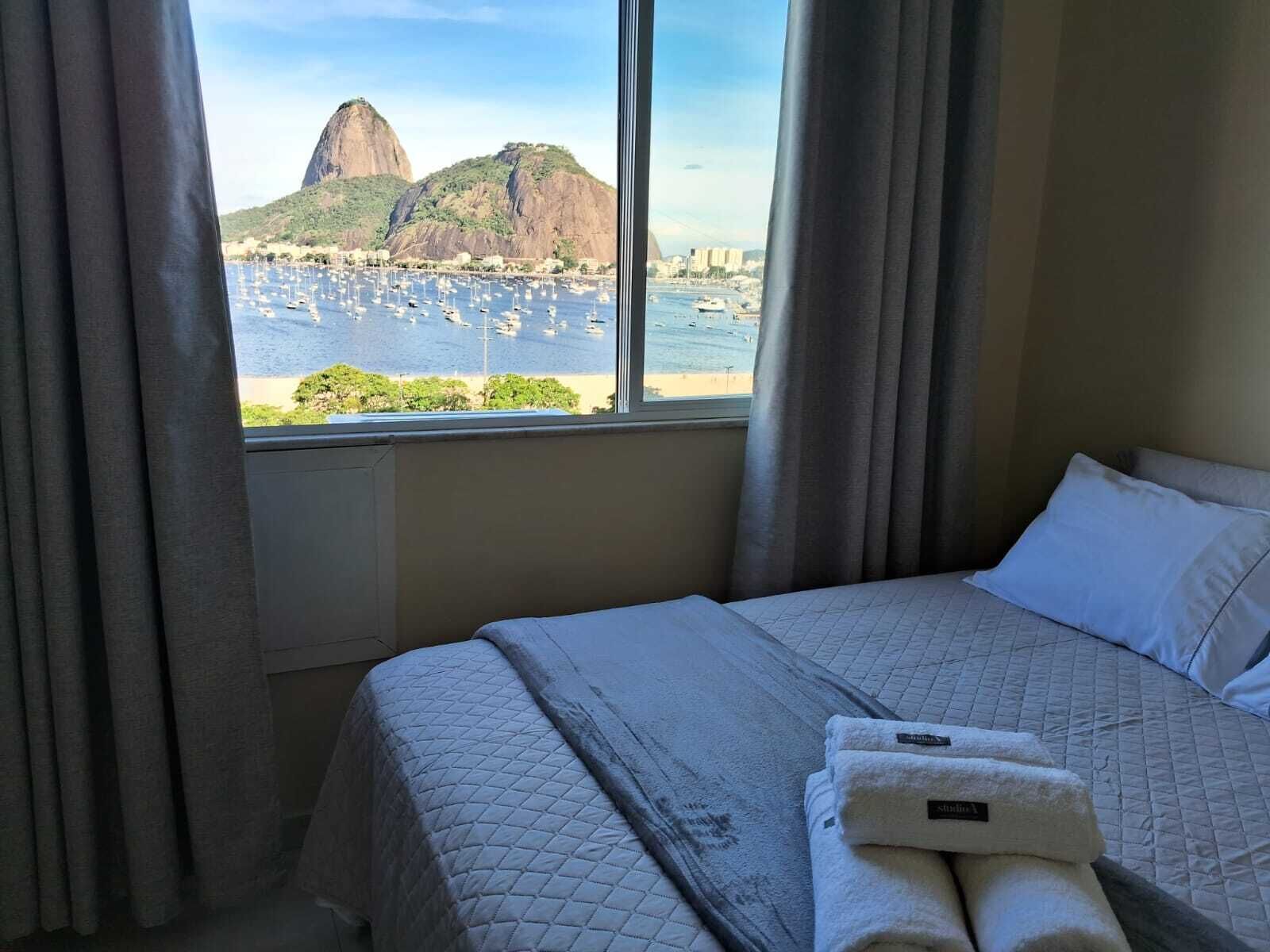 Ett hotellrum med en säng, ett fönster med gardiner och utsikt över ett berg och en småbåtshamn.