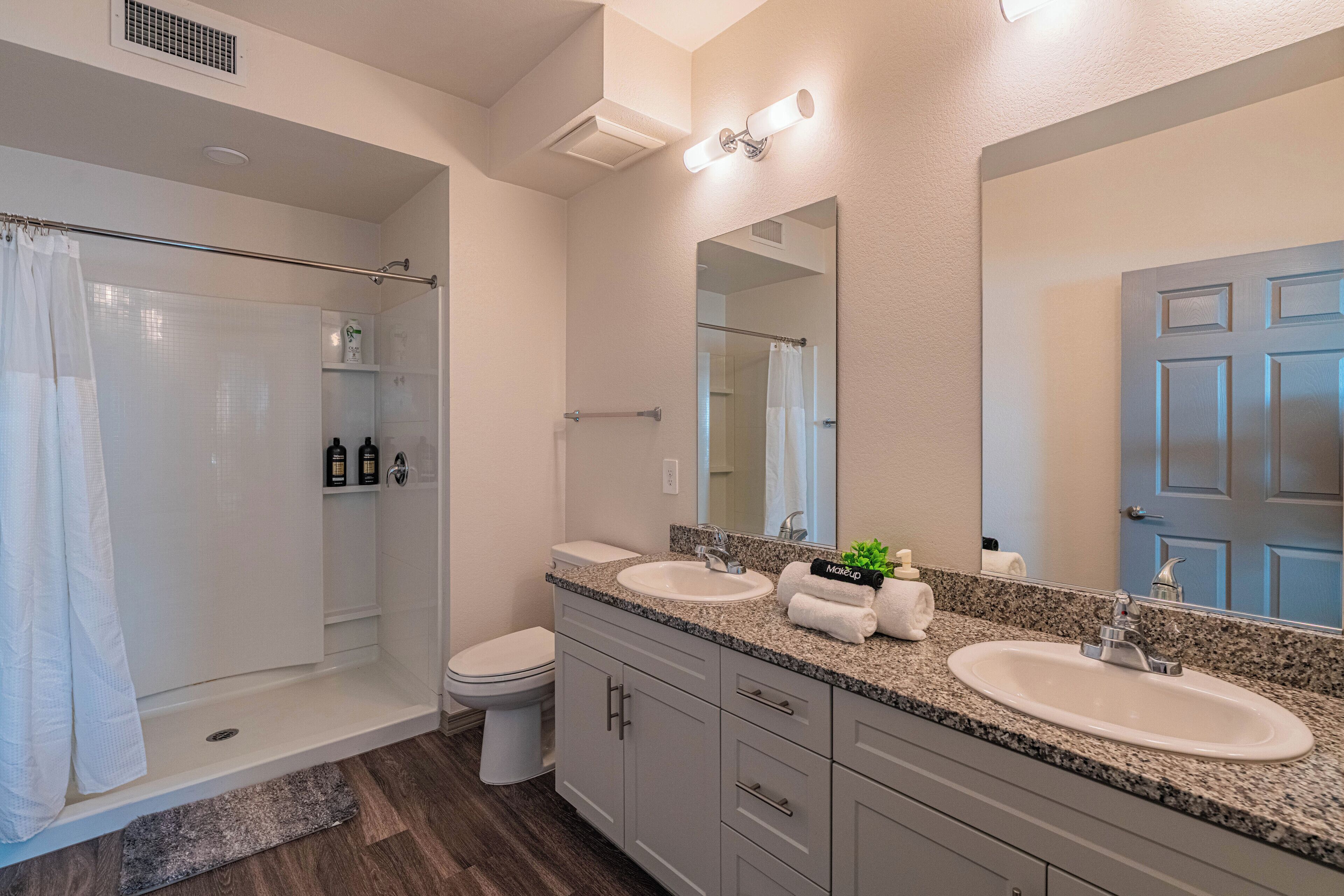 A modern bathroom with a glass shower enclosure, two sinks, a large mirror, and a toilet.