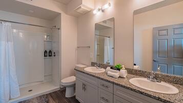 Un baño moderno con cabina de ducha de vidrio, dos lavamanos, un espejo grande y un inodoro.