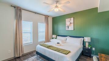 Un dormitorio con cama, mesitas de noche, ventilador de techo y una pared verde decorativa.