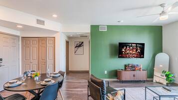 A dining area with a round table set for four, a television mounted on the wall, and a cabinet with children's toys.