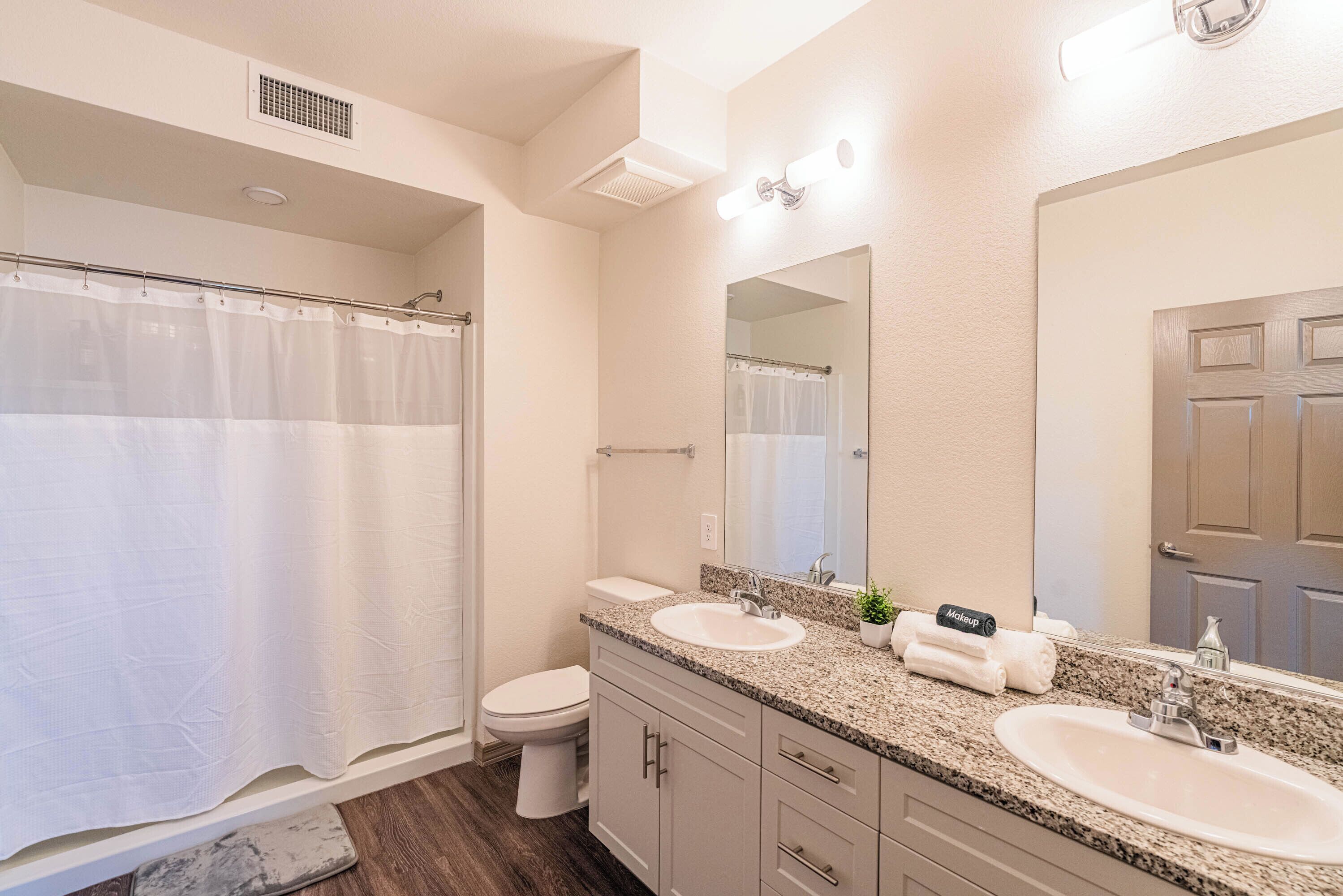 A bathroom with two sinks, a toilet, a shower curtain, and a large mirror.