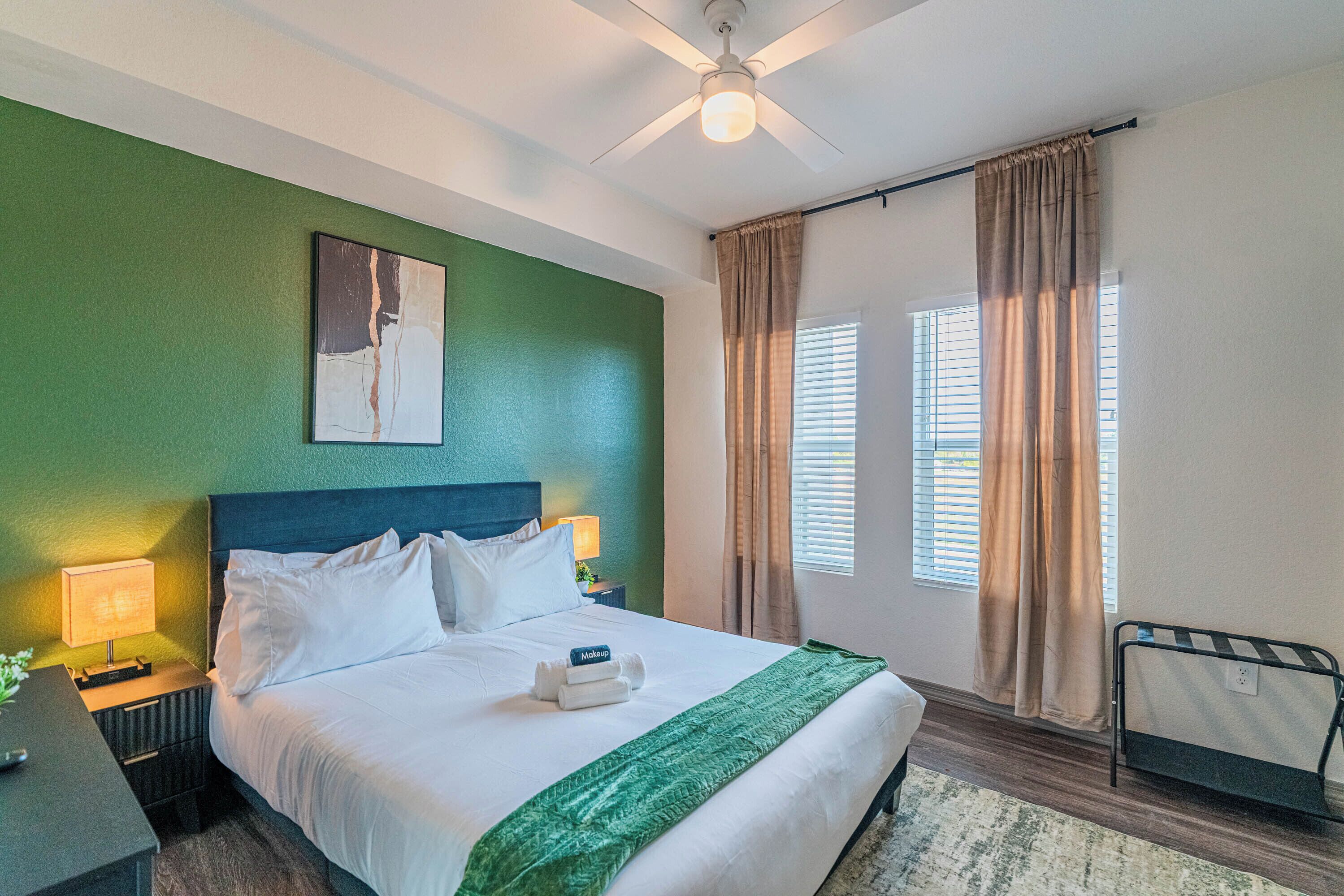 A hotel room with a bed, a nightstand, a lamp, a ceiling fan, and a window with curtains.