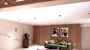 Ein modernes Wohnzimmer mit einem grünen Sofa, zwei Hocker, einer großen Topfpflanze und einer Holzvertäfelung.