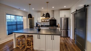 A modern kitchen with white cabinetry, a large island with stools, stainless steel appliances, and pendant lighting.