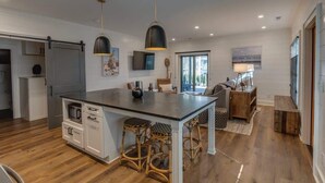A modern kitchen with a central island, wooden flooring, and a dining area with a sofa and table.