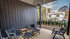 A covered outdoor seating area with four chairs and a table, wooden flooring, and a decorative light fixture.