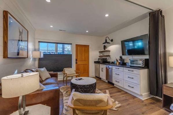 Una sala de estar moderna con sofá, mesa de centro y comedor con mostrador de cocina y microondas.