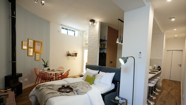 Ein modernes Hotelzimmer mit Bett, Nachttisch, Lampe und einem Essbereich mit Stühlen und Tisch.