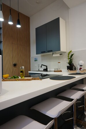 Una cocina moderna con encimera blanca, taburetes de bar, una planta en maceta y una cafetera.