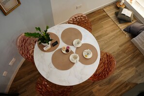 Ein runder Tisch mit weißer Marmorplatte, umgeben von gewebten Untersetzern, einer Zimmerpflanze und einem kleinen Teller mit einem Getränk.