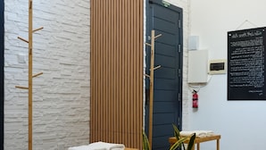 Een kamer met een houten bankje, een wandrek voor handdoeken, een potplant, een houten deur en een mat op de vloer.