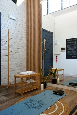Ein Zimmer mit einer hölzernen Bank, einem an der Wand befestigten Handtuchhalter, einem Topf mit Pflanze, einer Holztür und einer Matte auf dem Boden.