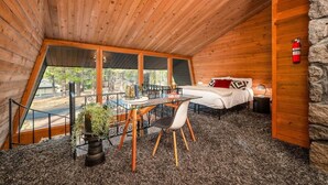 A cozy room with a bed, a dining table with chairs, and a large window offering a view of the outdoors. - The Mod Lodge, Retro Sunriver Cabin Vibes! (Sunriver)