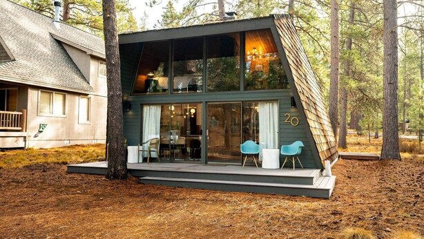 A modern house with a sloped roof, large glass windows, and a deck with chairs. - The Mod Lodge, Retro Sunriver Cabin Vibes! (Sunriver)