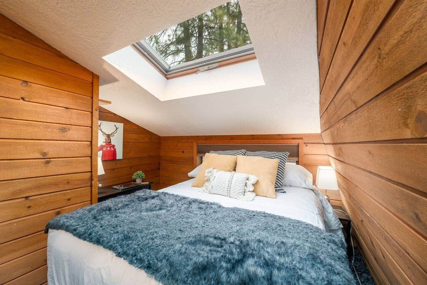 Een gezellige slaapkamer met dakraam, houten wanden, een bed met veel kussens en een klein nachtkastje.