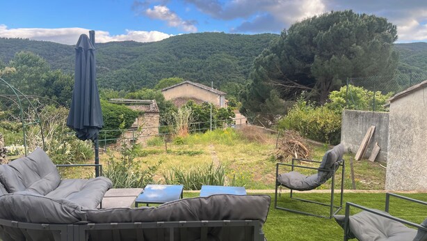 Une terrasse avec des meubles d’extérieur, une vue sur une maison et un paysage montagneux.
