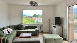 Un salon moderne avec un canapé vert, une table basse en bois, un lampadaire et un téléviseur posé sur un meuble.