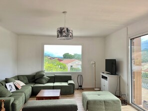 Un salon moderne avec un canapé vert, une table basse en bois, un lampadaire et un téléviseur posé sur un meuble.