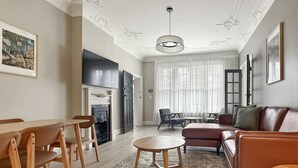A living room with a fireplace, a dining area with wooden chairs, a sofa, and a TV mounted on the wall. - The Edward Residences Quiet Luxury (North Sydney)