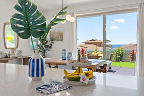 Zona de menjador amb taula preparada per a dues persones, una gran planta tropical i un plat de fruita amb un plàtan i una flor.