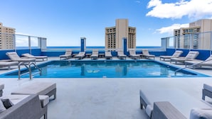 Ein Pool auf dem Dach mit Liegestühlen und Blick auf das Meer und die Gebäude.