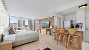 Ein modernes Hotelzimmer mit einem großen Bett, einer Essecke mit Barhocker, einer Küche und Blick auf die Stadt.