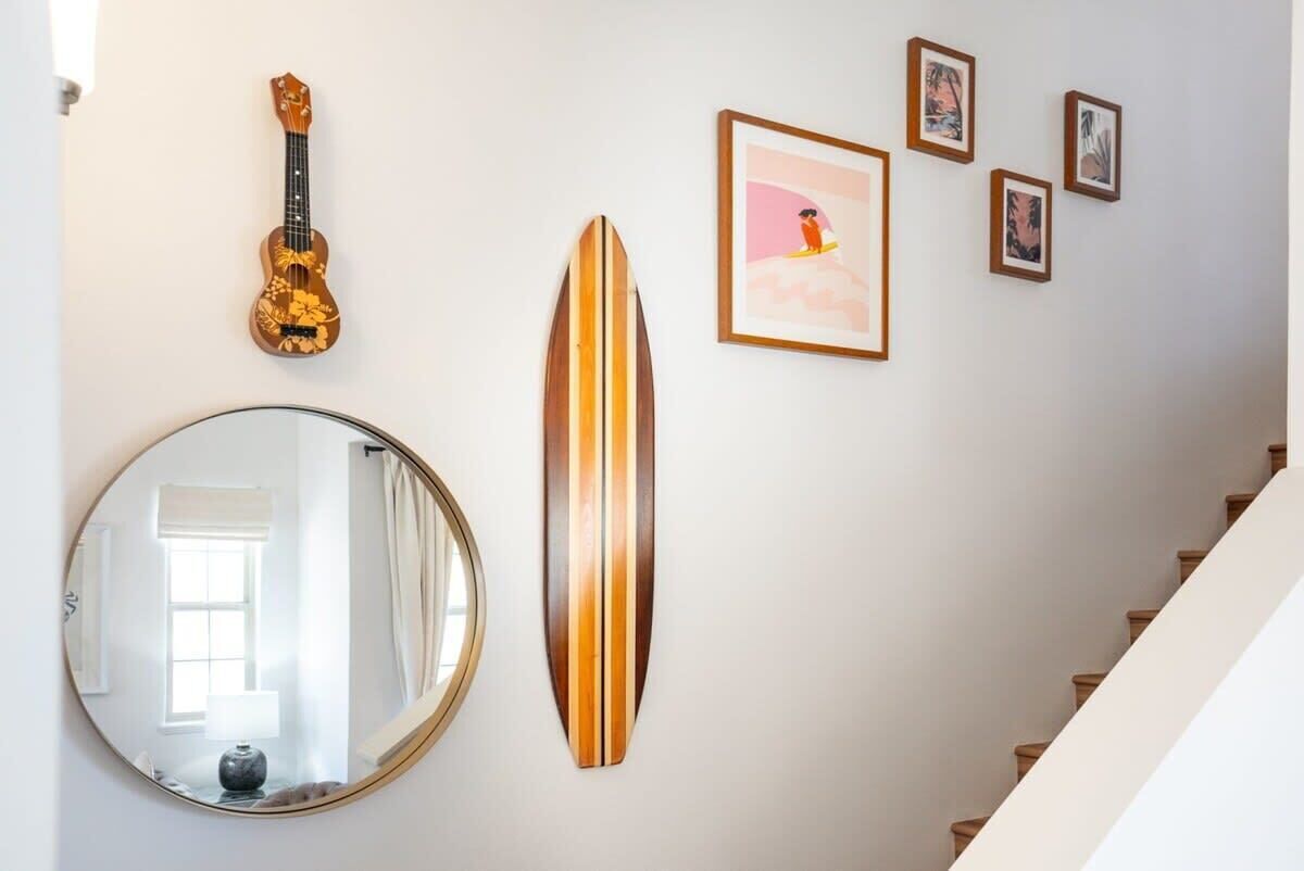 A staircase with a wooden handrail and a wall decorated with a ukulele, a surfboard, and framed pictures.