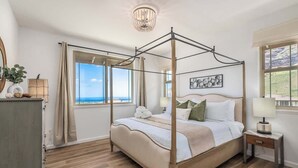 Een hemelbed met uitzicht op zee, een kroonluchter en een nachtkastje met een lamp.