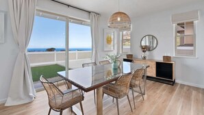 Een eethoek met een glazen tafel, rieten stoelen, een hanglamp en uitzicht op de oceaan.