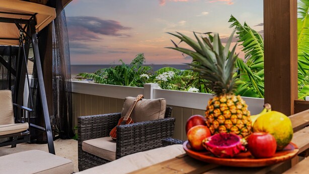 A patio with wicker furniture, a guitar, and a fruit bowl with pineapple, apple, and dragon fruit. - @ Marbella Lane - Stunning Gem w/ MT & Ocean Views (Waianae)