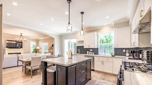 A modern kitchen with a central island, white cabinetry, and a large window providing natural light.