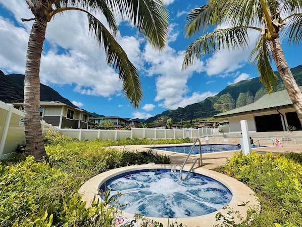 A hot tub surrounded by lush greenery and palm trees, with a pool and a view of mountains in the background.