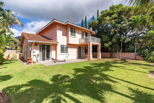 A two-story house with a balcony, a covered patio, and a well-maintained lawn.