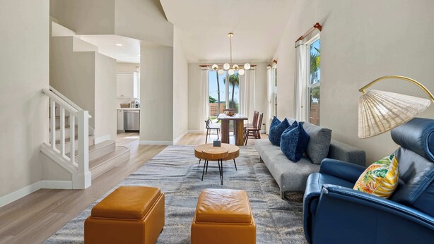 A spacious living area with a sofa, ottomans, a dining table, and a staircase.