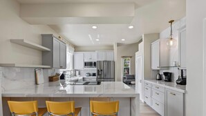 A modern kitchen with white cabinetry, a marble countertop, and yellow bar stools.