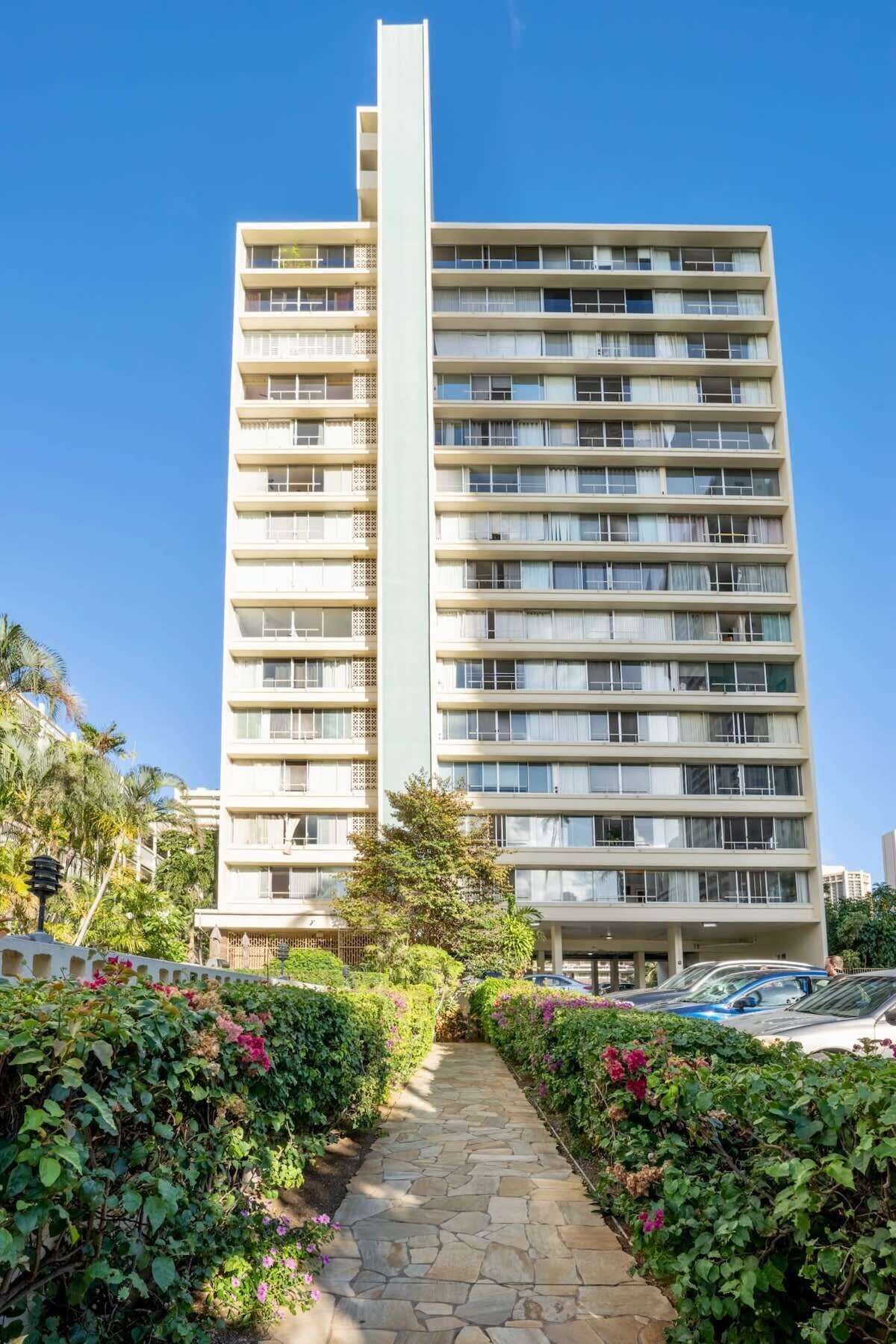 Un hotel de gran altura con varios balcones, un elemento vertical central y un camino de piedra que conduce a la entrada.