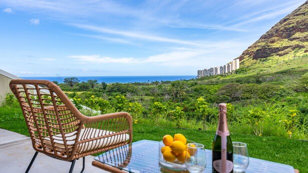 Ein Korbstuhl und ein Tisch mit einer Champagnerflasche, Zitronen und einem Glas auf einem Balkon mit Blick auf eine üppige Landschaft und den Ozean.