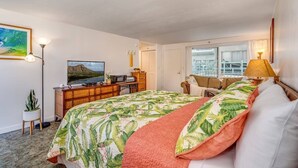 Ein Schlafzimmer mit Bett, Schreibtisch, Fernseher, Fenster und einer Pflanze.