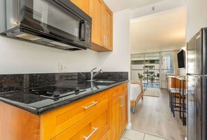 Una cocina moderna con armarios de madera, encimera negra, microondas de acero inoxidable y horno empotrado.